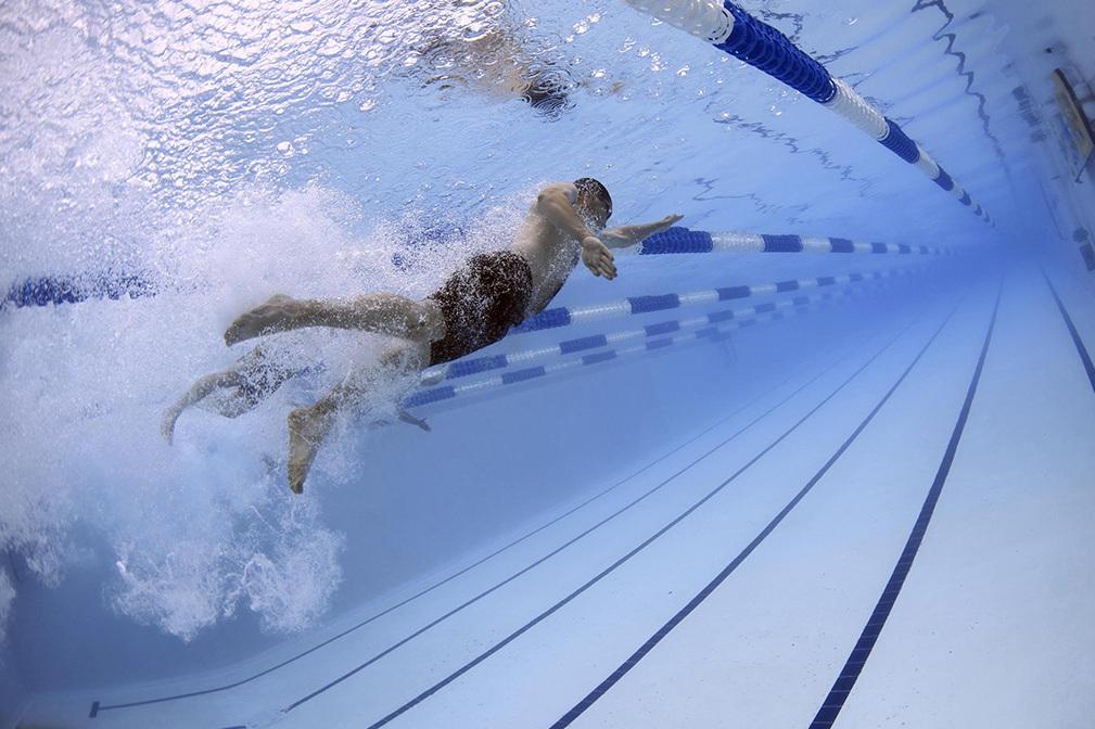 Schwimmer unter Wasser, der an einer blauen Bahn in einem Schwimmbecken vorbeizieht, mit Wellenbildung um ihn herum.
