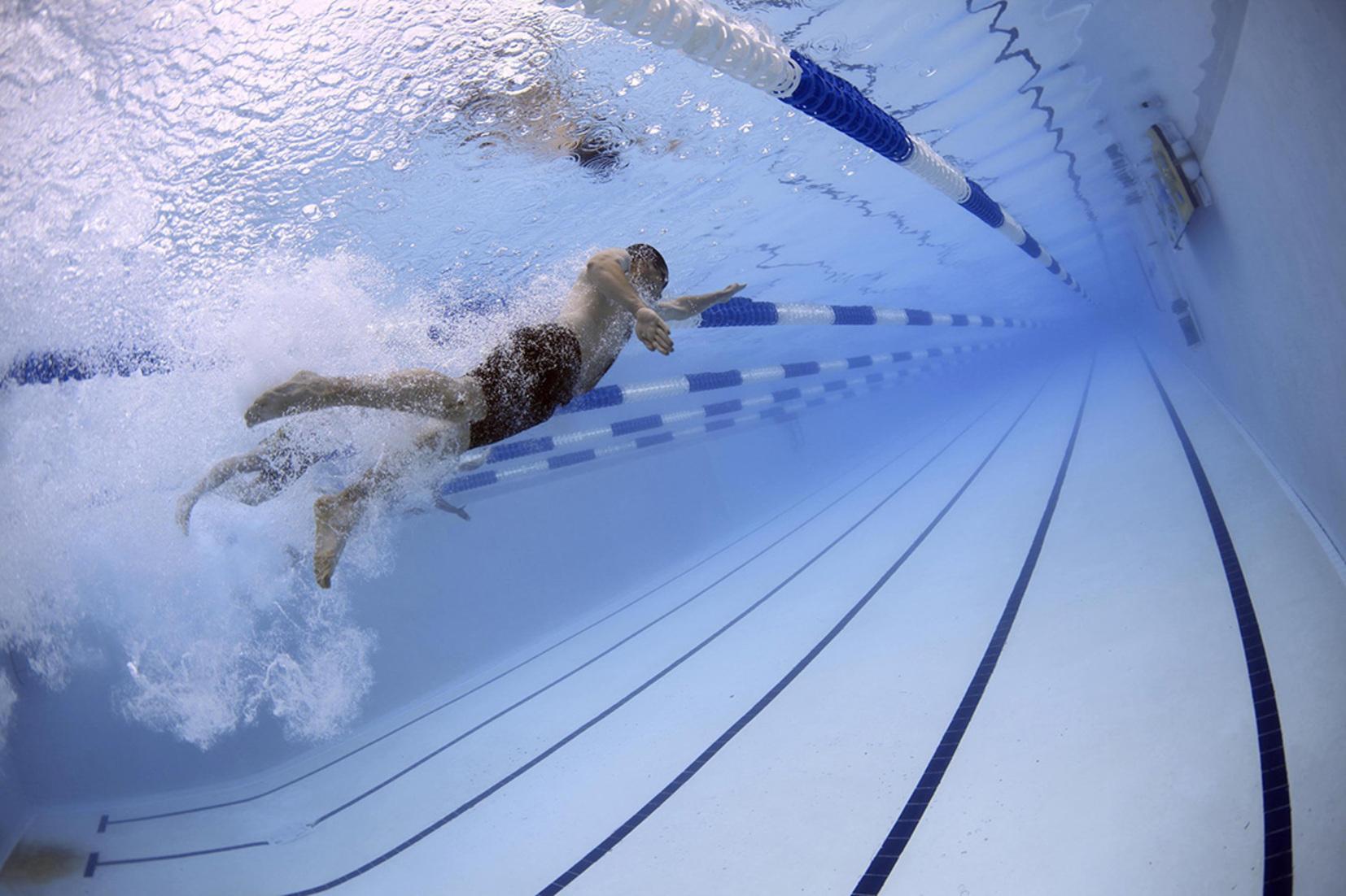 Schwimmer unter Wasser, der an einer blauen Bahn in einem Schwimmbecken vorbeizieht, mit Wellenbildung um ihn herum.
