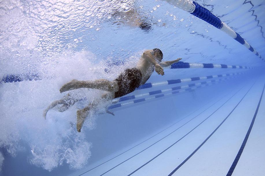 Schwimmer unter Wasser, der an einer blauen Bahn in einem Schwimmbecken vorbeizieht, mit Wellenbildung um ihn herum.