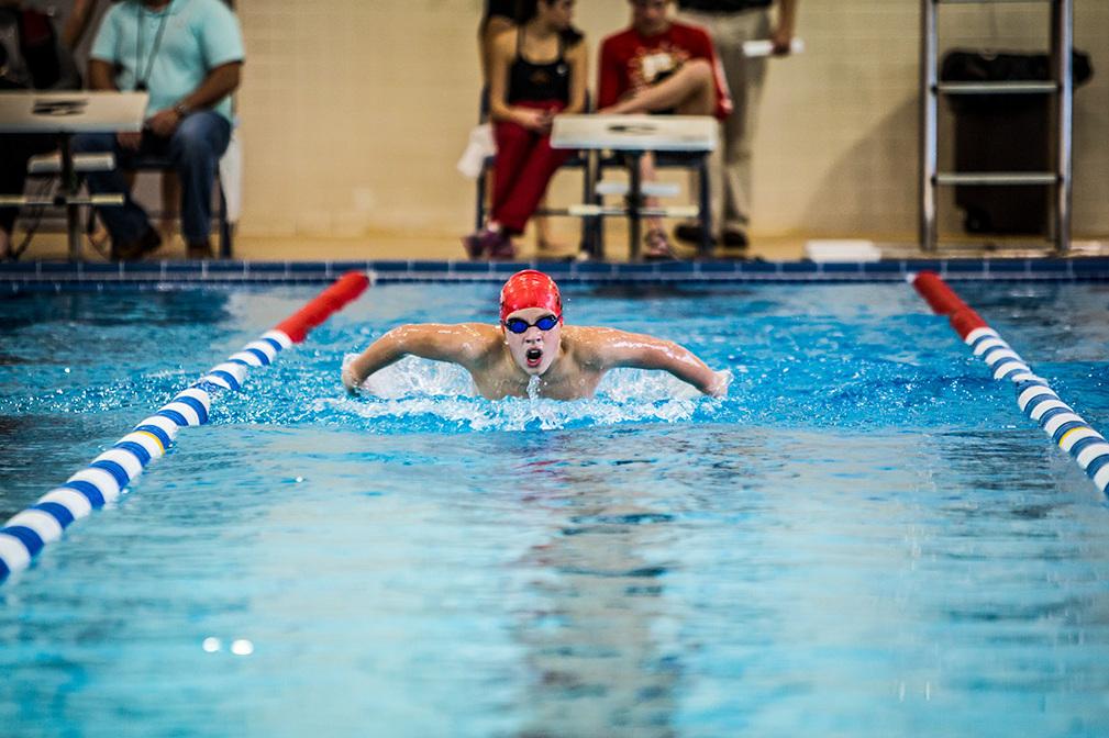 Schwimmer in roter Badekappe und Brille Brustschwimmen im blauen Schwimmbecken, Zuschauer im Hintergrund.