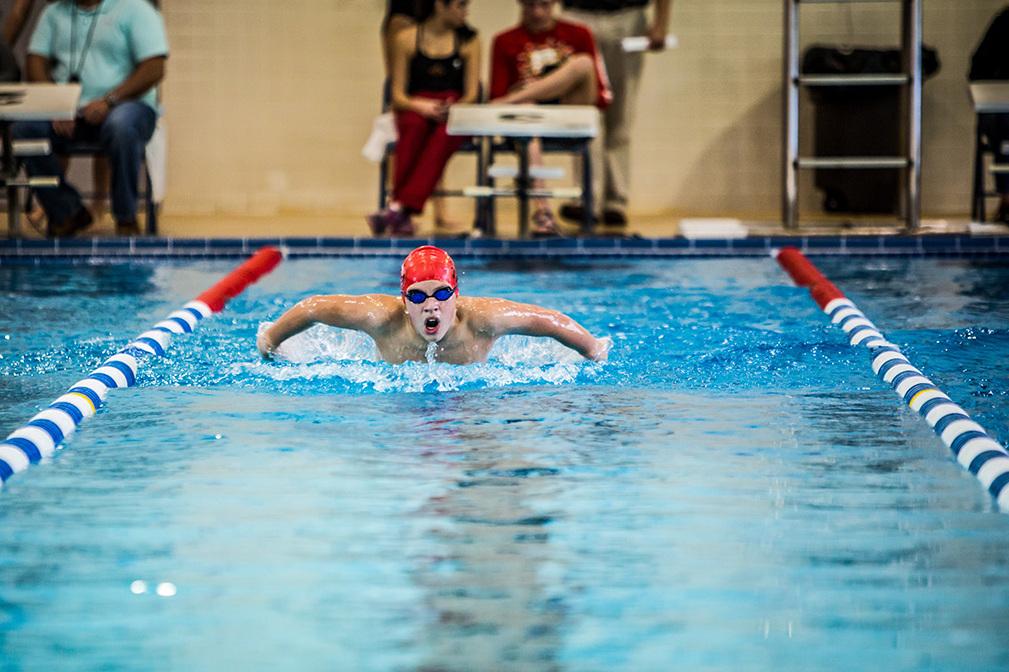 Schwimmer in roter Badekappe und Brille Brustschwimmen im blauen Schwimmbecken, Zuschauer im Hintergrund.