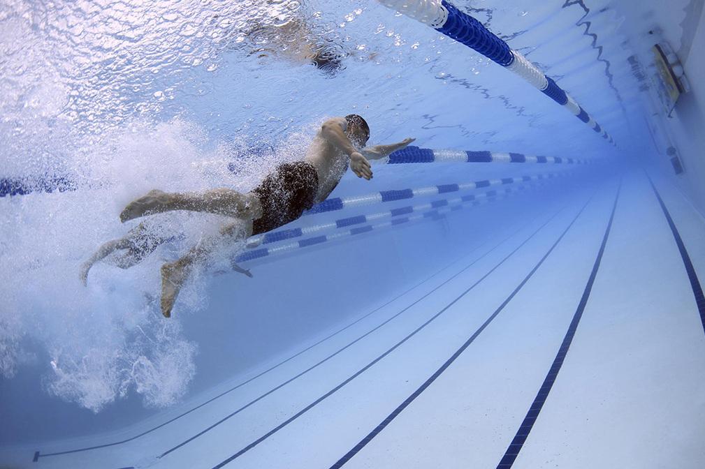 Schwimmer unter Wasser, der an einer blauen Bahn in einem Schwimmbecken vorbeizieht, mit Wellenbildung um ihn herum.