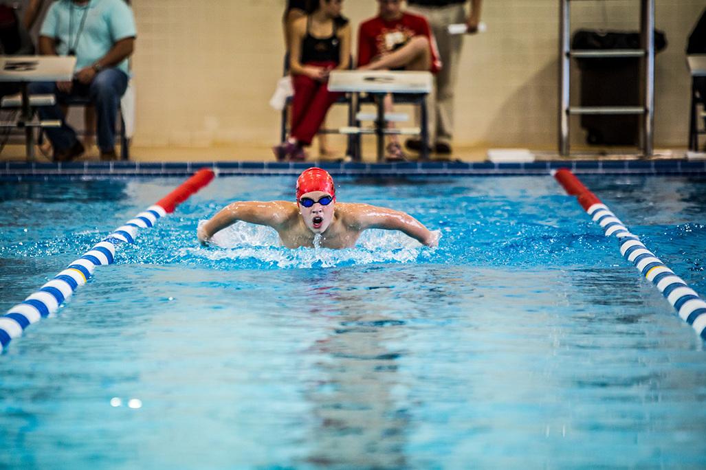 Schwimmer in roter Badekappe und Brille Brustschwimmen im blauen Schwimmbecken, Zuschauer im Hintergrund.