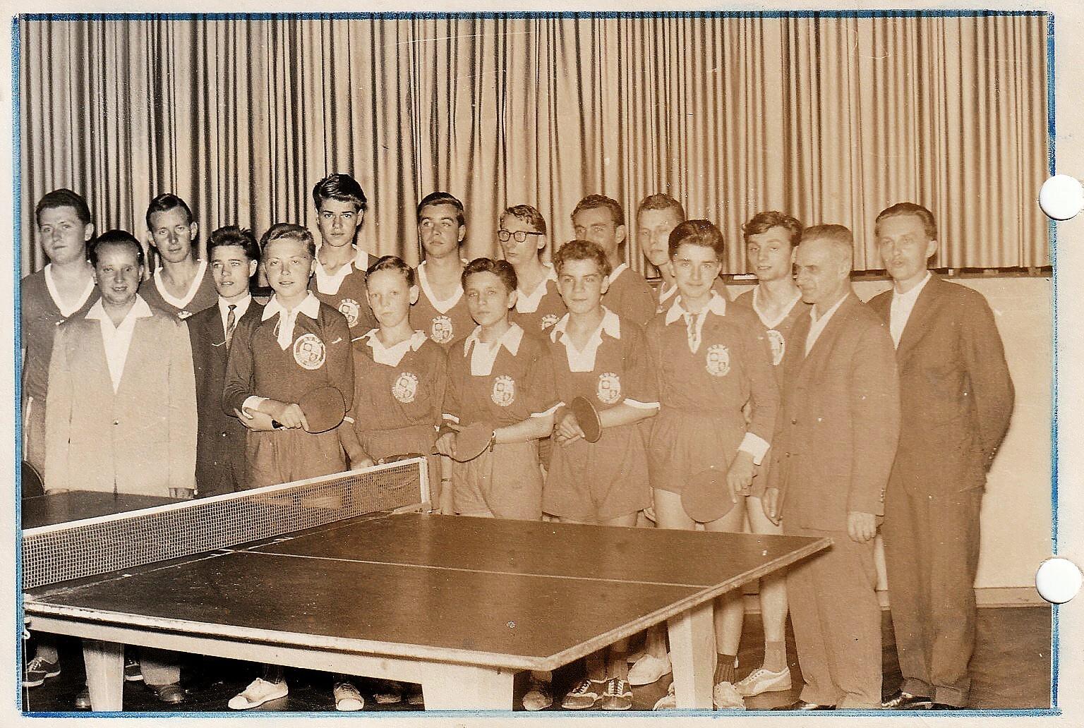 Gruppenfoto von Tischtennisspielern in einheitlichen Pullovern, posierend vor einem Tischtennistisch in einem Saal.