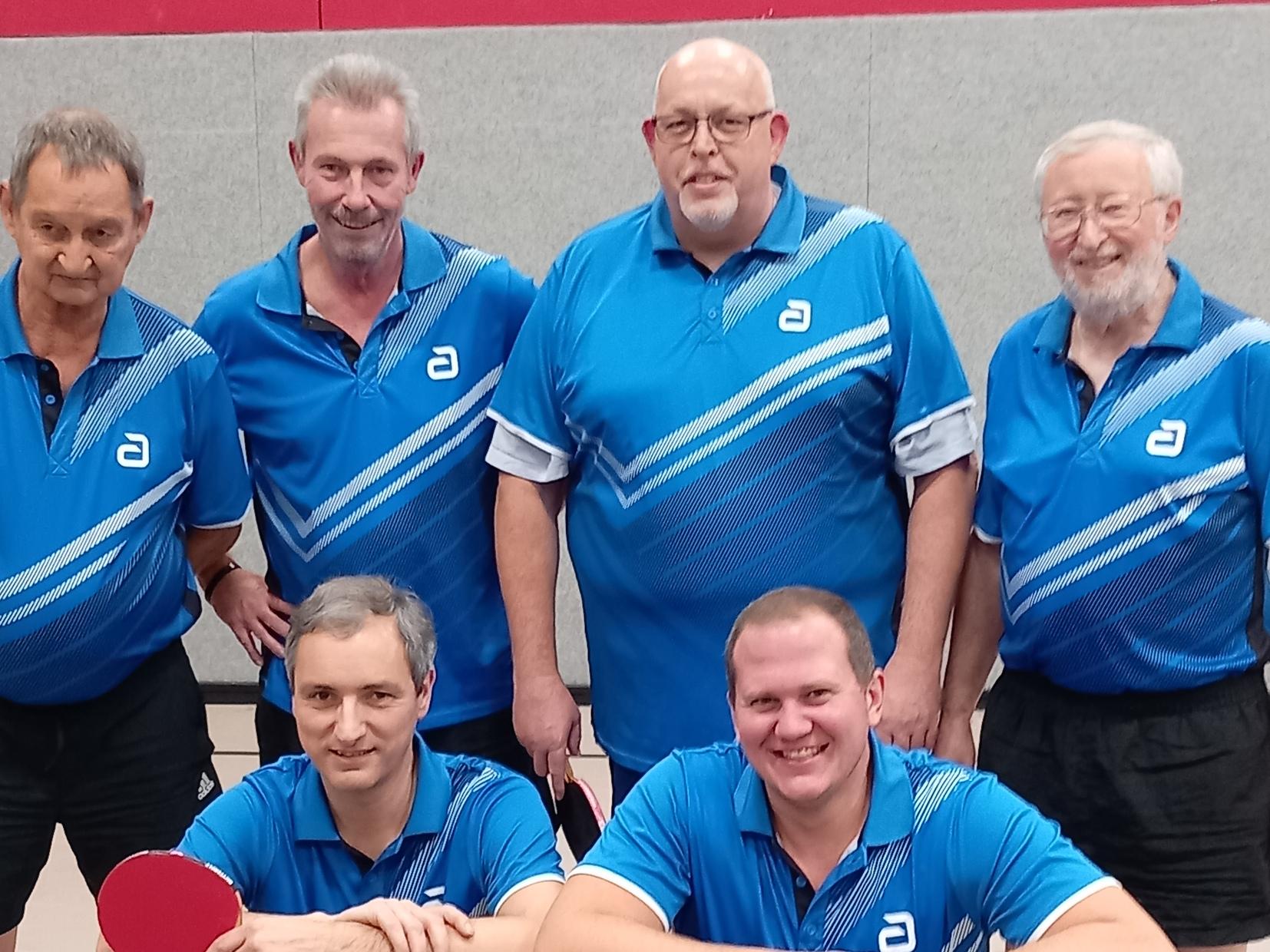 Sechs Tischtennisspieler posieren in blauen Trikots vor einem Tischtennistisch mit einem Schl&auml;ger und Ball.