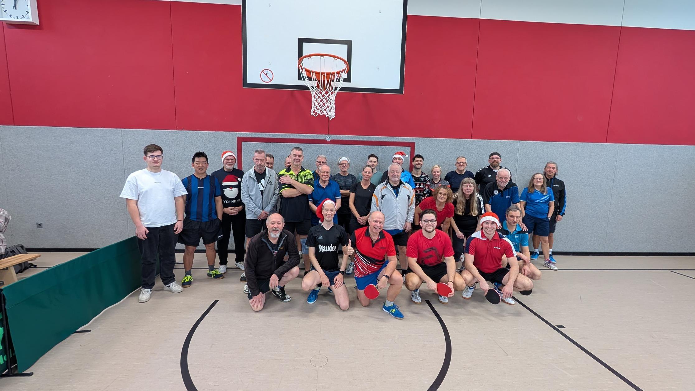 Gruppenfoto von Tischtennisspielern in einer Sporthalle, einige tragen Weihnachtsmützen, Tischtennisschläger in der Hand.
