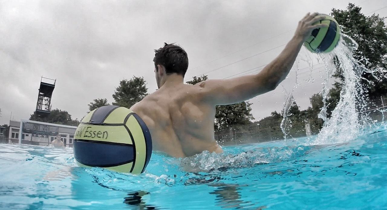 Wasserspiele: Mann mit Wasserball im Pool, mit nur teilweise sichtbarem R&uuml;cken und Spritzwasser im Fokus.