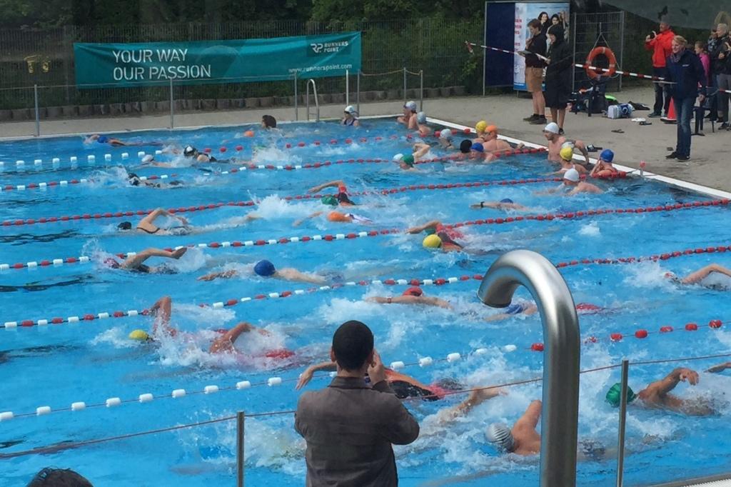 Gruppenschwimmen in einem Freibad mit mehreren Sportlern, die in verschiedenen Schwimmstilen um eine Bahn schwimmen.