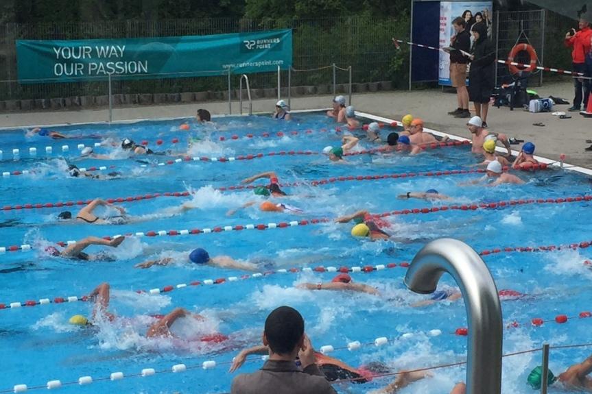 Gruppenschwimmen in einem Freibad mit mehreren Sportlern, die in verschiedenen Schwimmstilen um eine Bahn schwimmen.