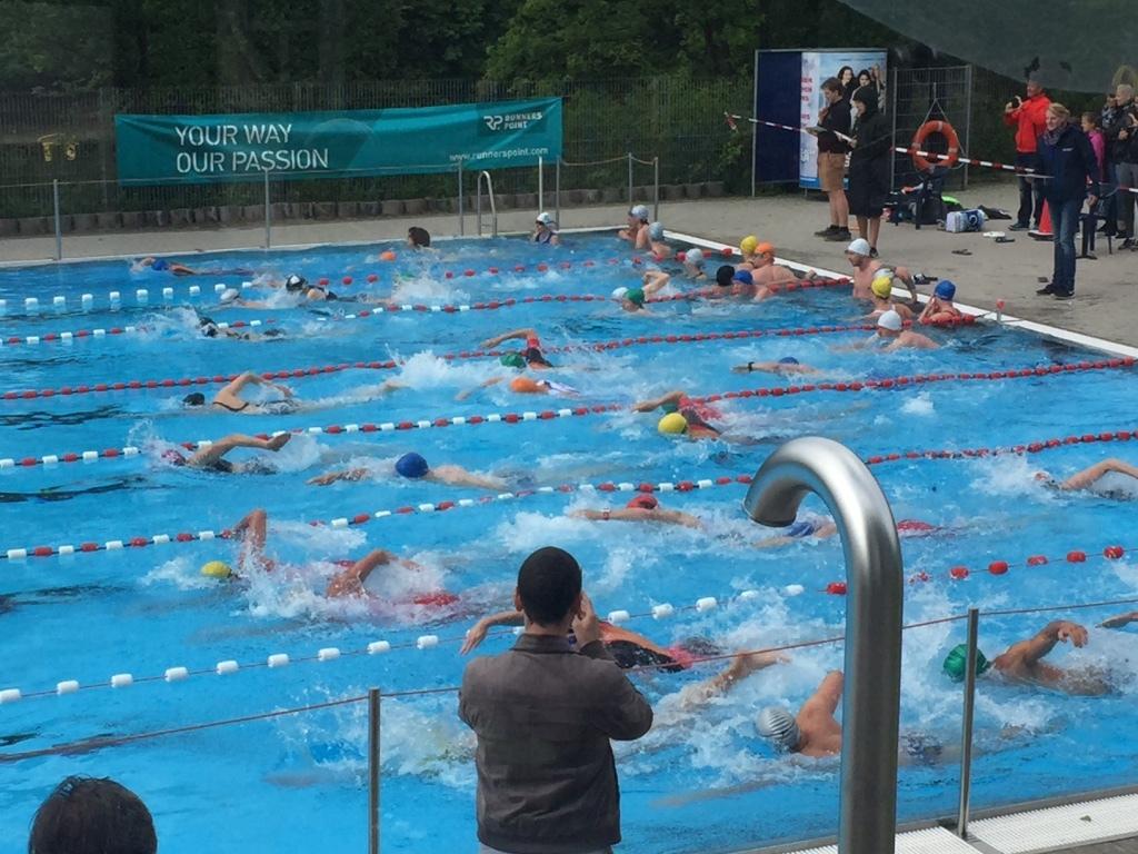 Gruppenschwimmen in einem Freibad mit mehreren Sportlern, die in verschiedenen Schwimmstilen um eine Bahn schwimmen.