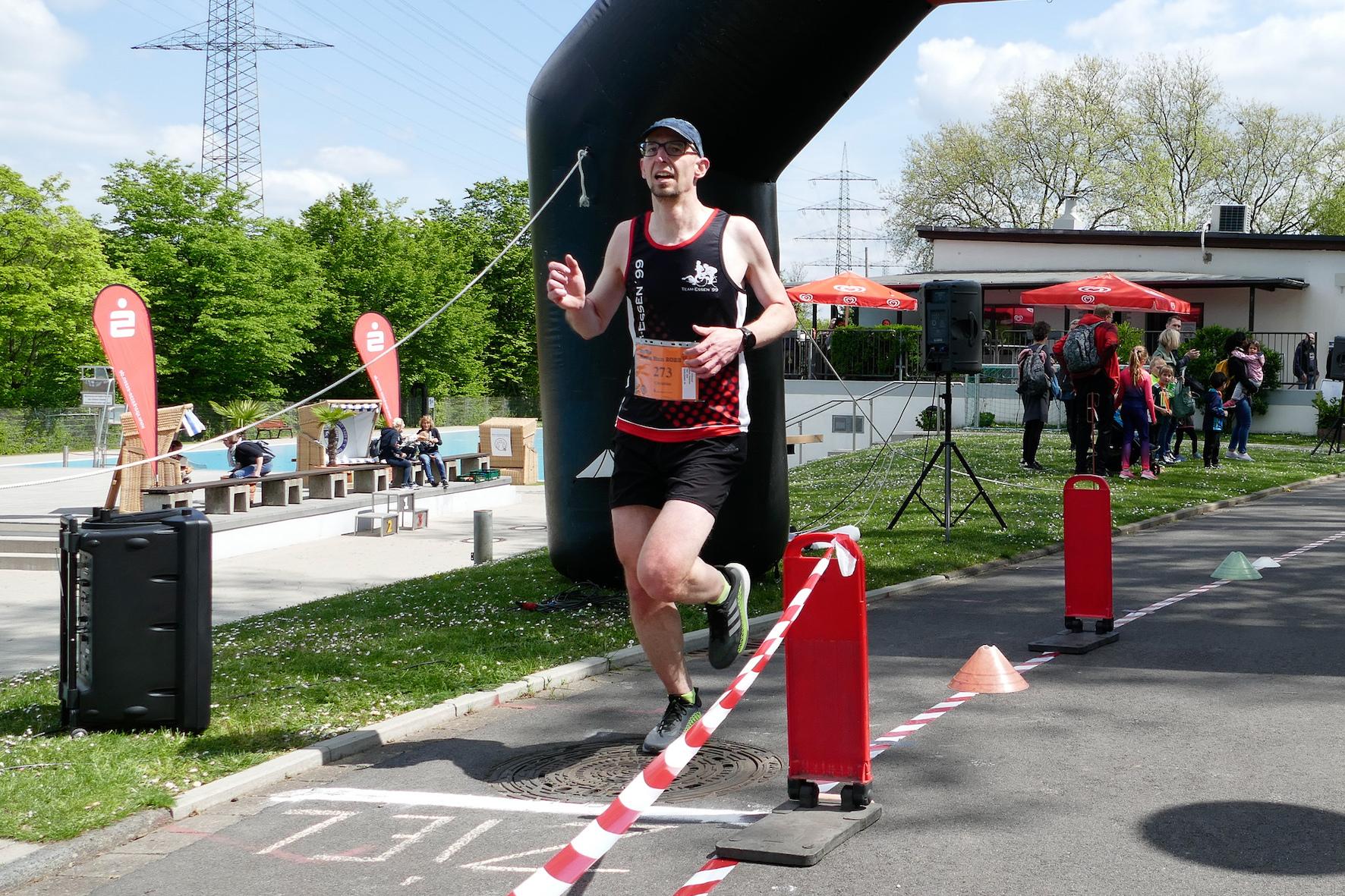L&auml;ufer &uuml;berquert das Ziel unter einem gro&szlig;en Tor und passierenden Zuschauern bei einem Sportevent.