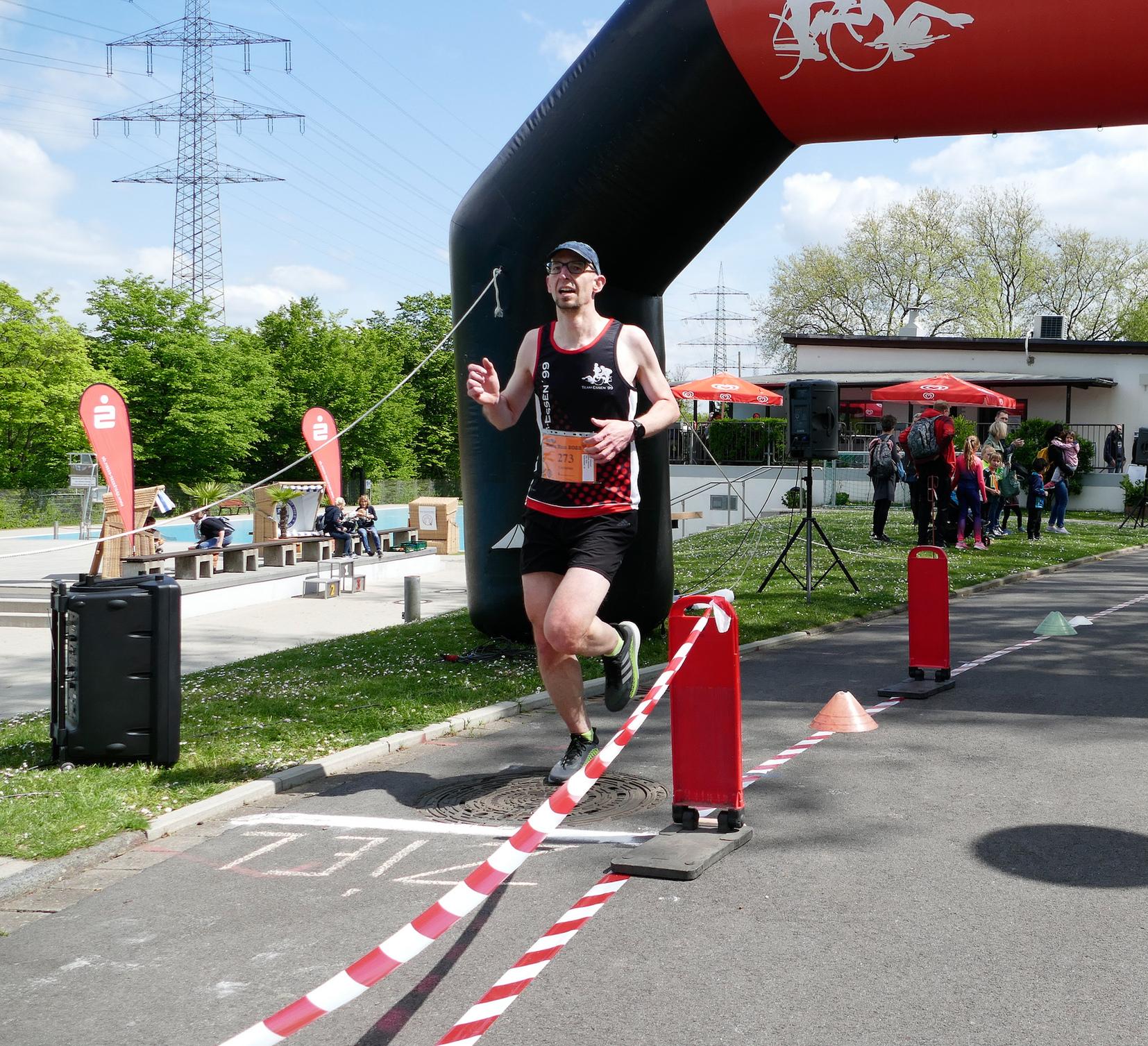 Läufer überquert das Ziel unter einem großen Tor und passierenden Zuschauern bei einem Sportevent.