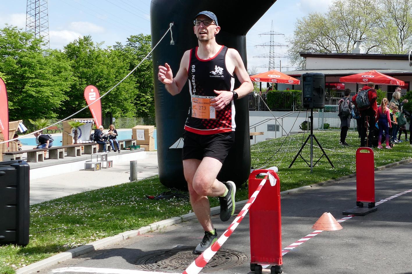 Läufer überquert das Ziel unter einem großen Tor und passierenden Zuschauern bei einem Sportevent.