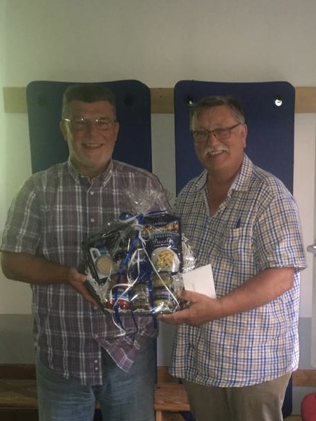 Zwei M&auml;nner l&auml;cheln und halten einen Geschenkkorb mit blauen und wei&szlig;en Dekorationen in einem Innenraum.