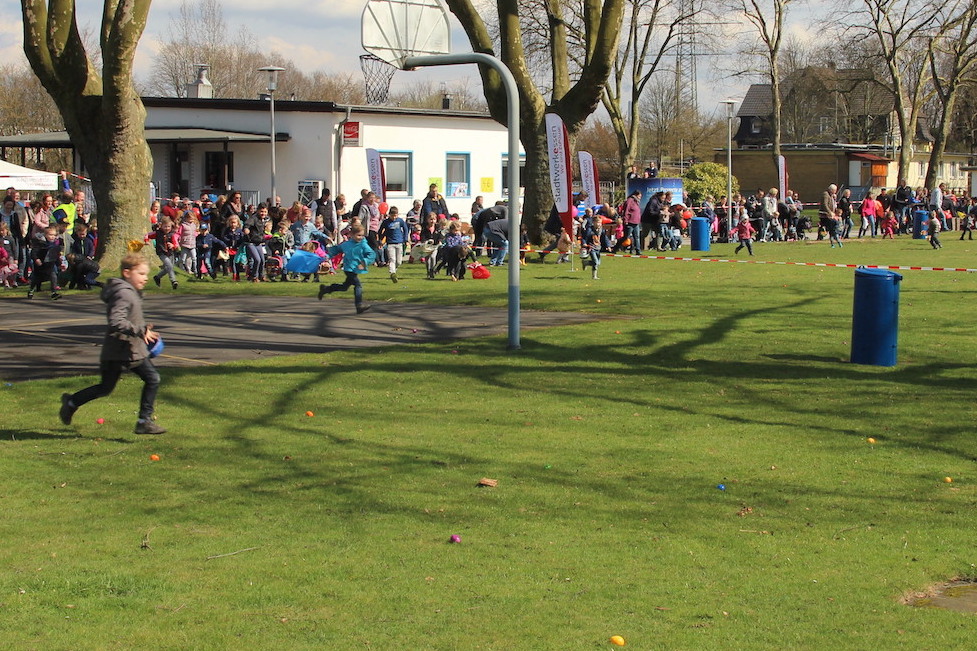 Kinder laufen auf einer Wiese, im Hintergrund ist eine gro&szlig;e Menschenmenge und ein Veranstaltungszelt zu sehen.