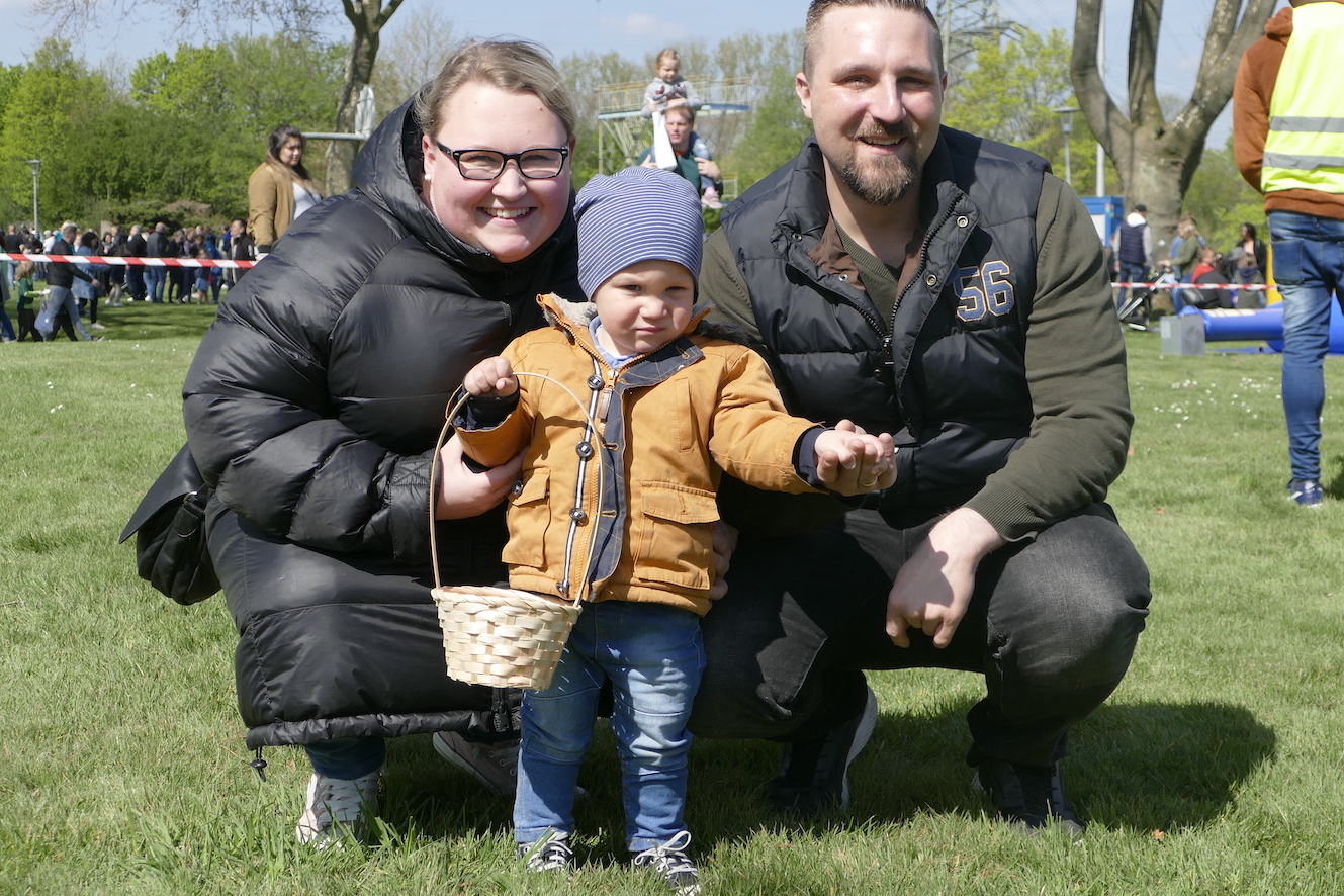 Familie mit einem Kleinkind in der Mitte, das einen Korb h&auml;lt, steht auf einer Wiese an einem sonnigen Tag.