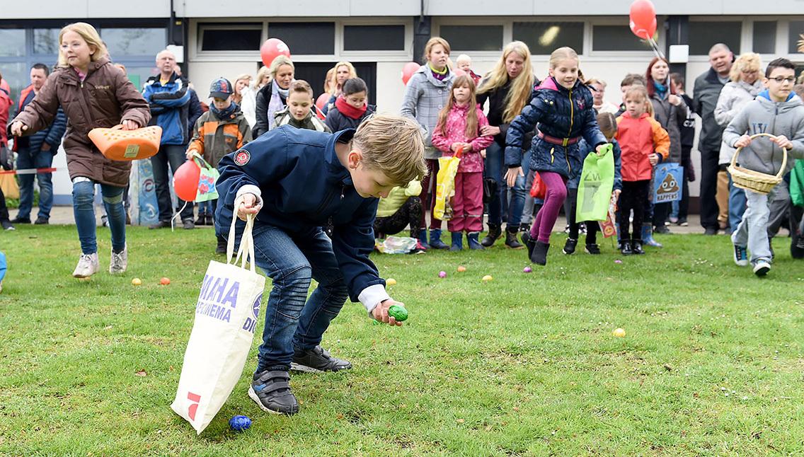 Kinder sammeln bunte Ostereier auf einem Rasen während einer Veranstaltung, umgeben von Erwachsenen und anderen Kindern.