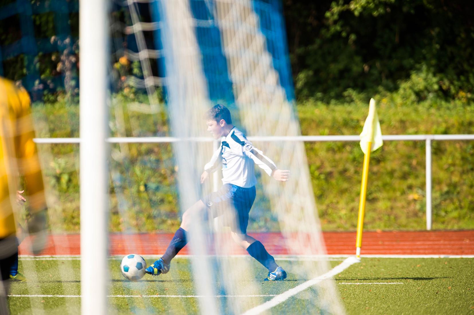 Wettkampf auf dem Fußballplatz: Ein Spieler in weiß-blauer Trikotausstattung schießt einen Ball ins Spiel.