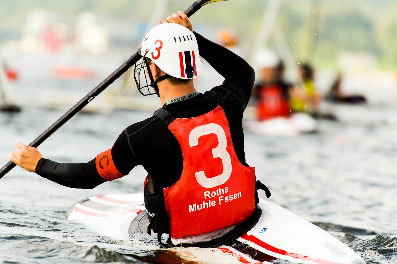 Kanute mit Helm paddelt auf einem Gewässer, trägt eine rote Weste mit der Nummer 3 und firmiert "Rothe Muhle Fssen".
